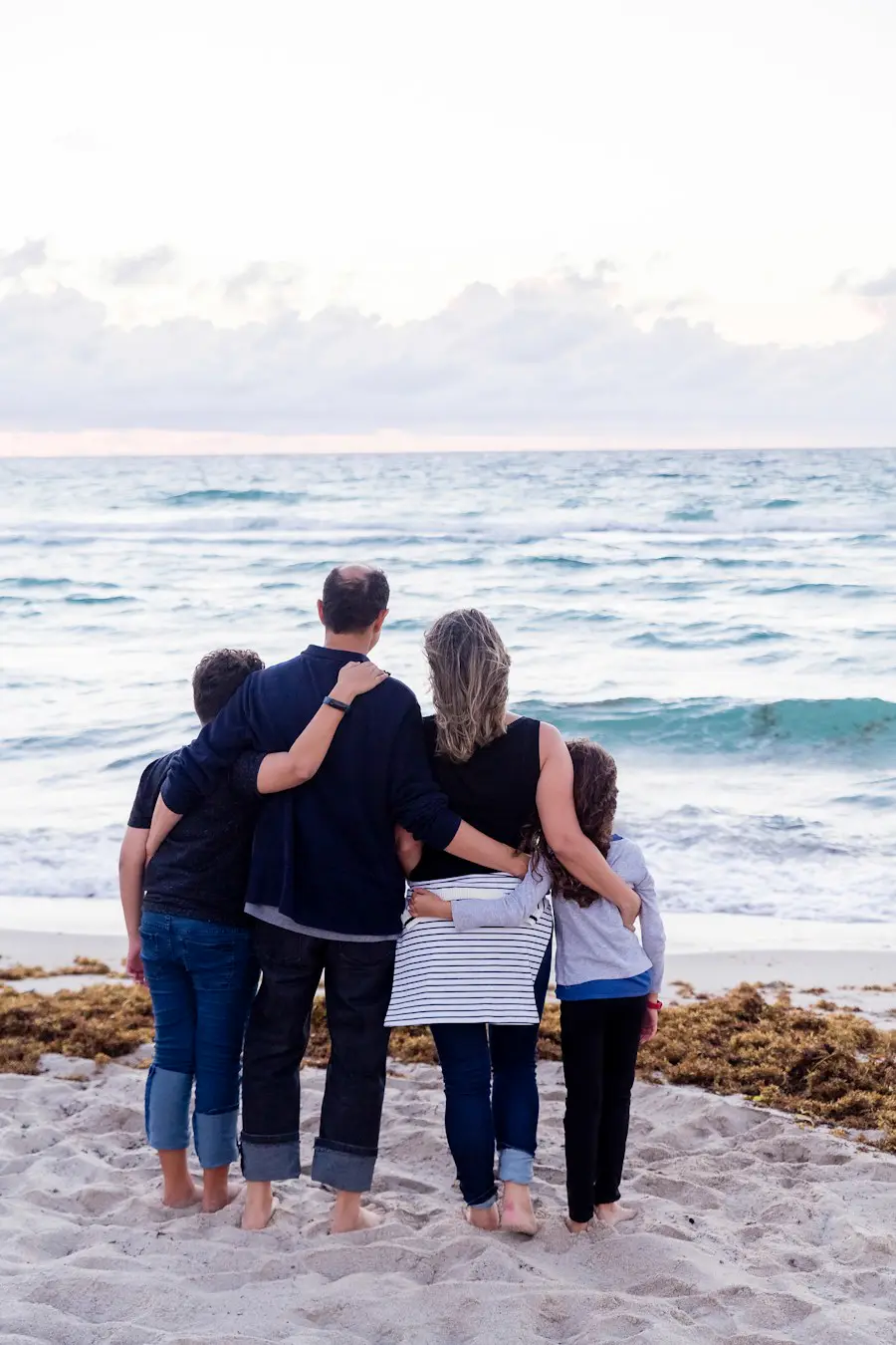 A family standing together on a beach, looking out at the ocean